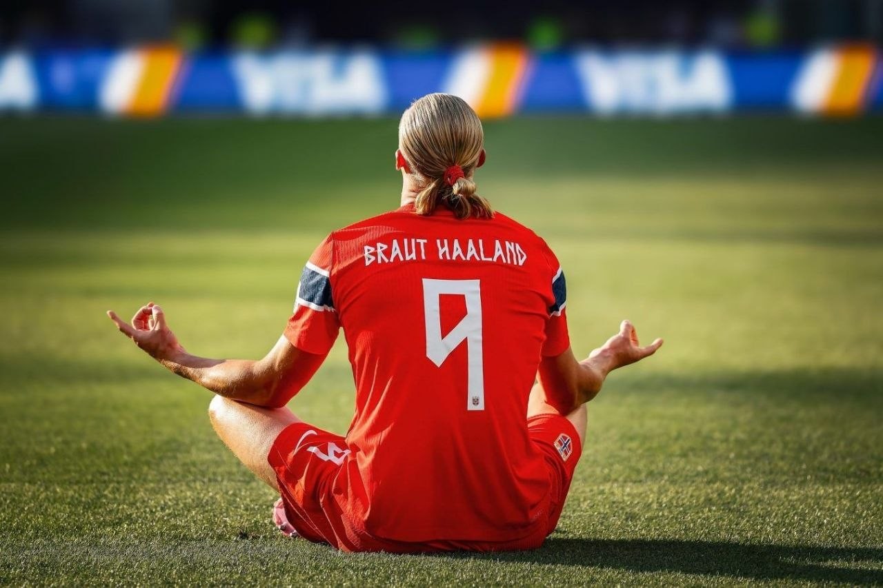 Erling Haaland sentado sobre el césped con la camiseta roja de Noruega