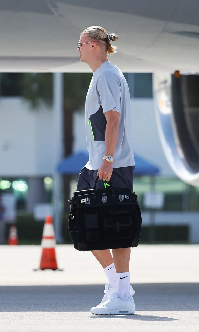 Erling Haaland caminando por un aeropuerto con un bolso Hermès negro